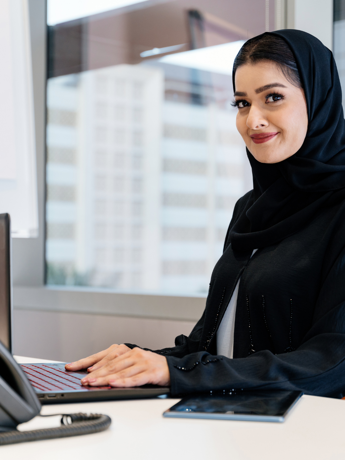 Woman wearing a black hijab sitting at a desk with a laptop thinking